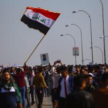 علم عراقي يرفرف في مظاهرة وسط حشد من الطلاب، وأحد الطلاب يلتقط صورة للعلم من الأسفل. 